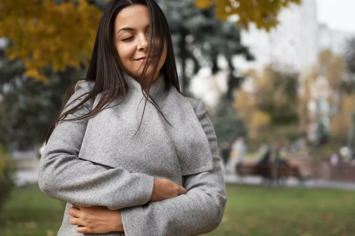 Woman in grey sweater finds tranquility in autumn park setting.