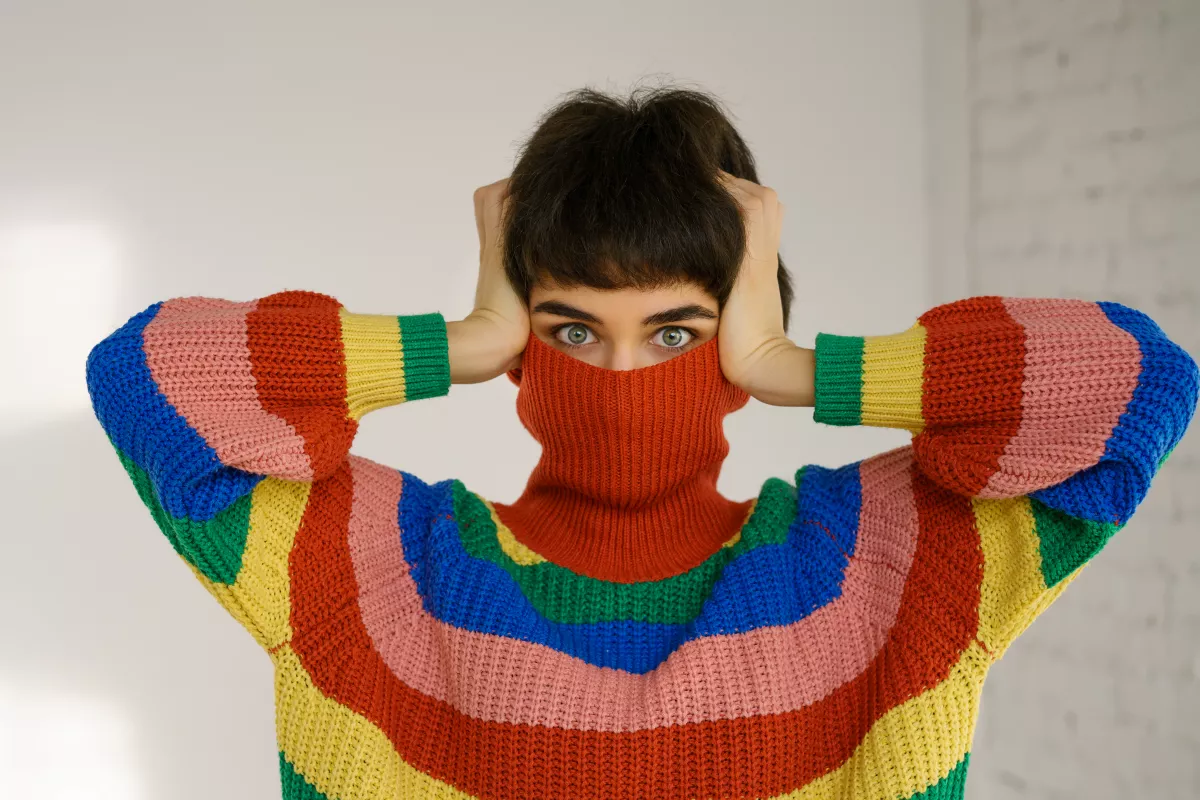 Person in a playful pose wearing a bright, striped knit sweater.