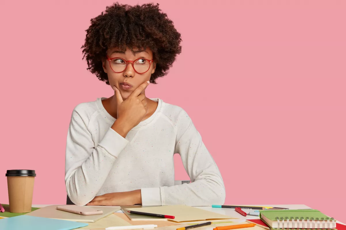 Contemplative person at pink desk with colorful outfit and thoughtful expression.
