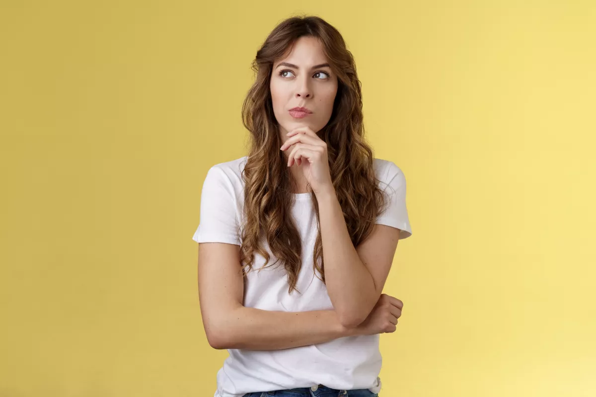 Young woman in casual attire deep in thought against vibrant yellow backdrop.