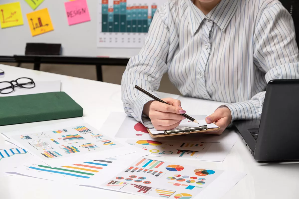 Professional analyzing data with charts, laptop, and notes in office workspace.
