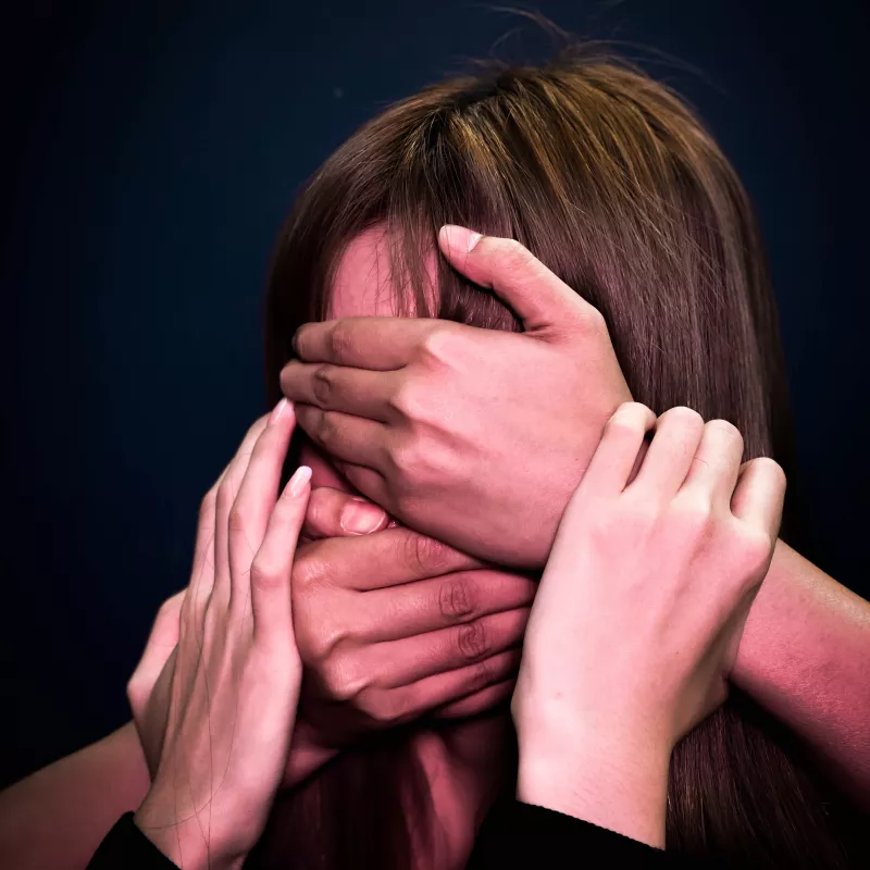 Multiple hands cover a face, symbolizing anonymity and external influence.