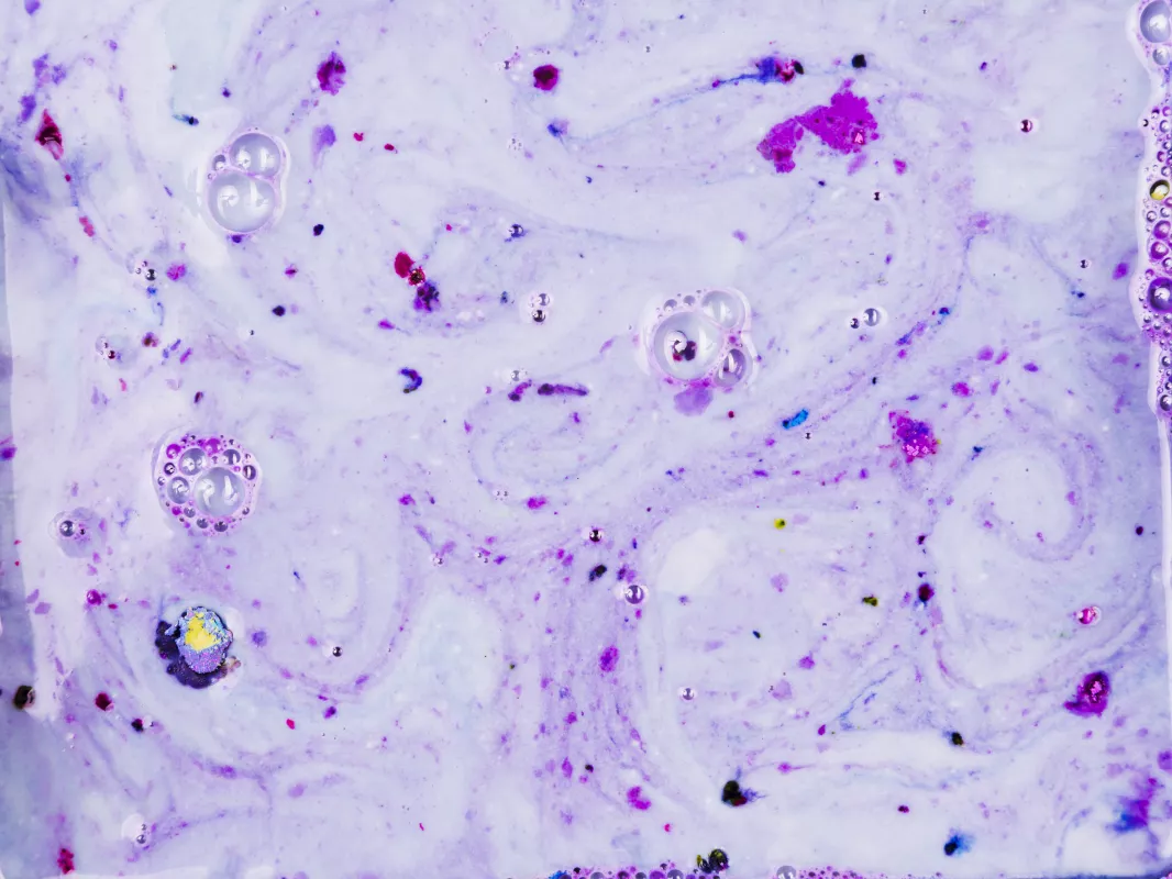 Close-up of a marbled lavender CBD bath bomb with colorful splashes and reflective bubbles.