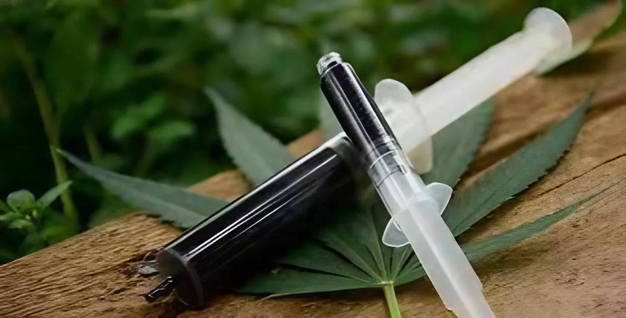 Medical cannabis consumption methods with syringe and vape pen on vibrant leaf.