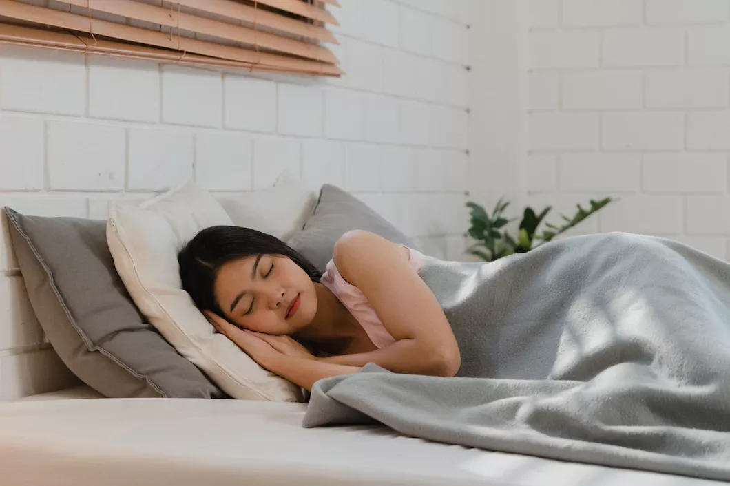 Woman resting in serene bedroom with soft bedding and natural light for a restful sleep.