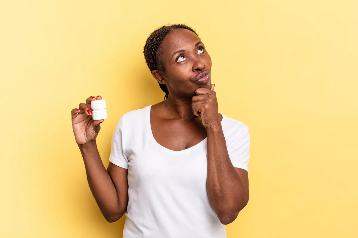 Person pondering CBD capsule benefits against yellow background.