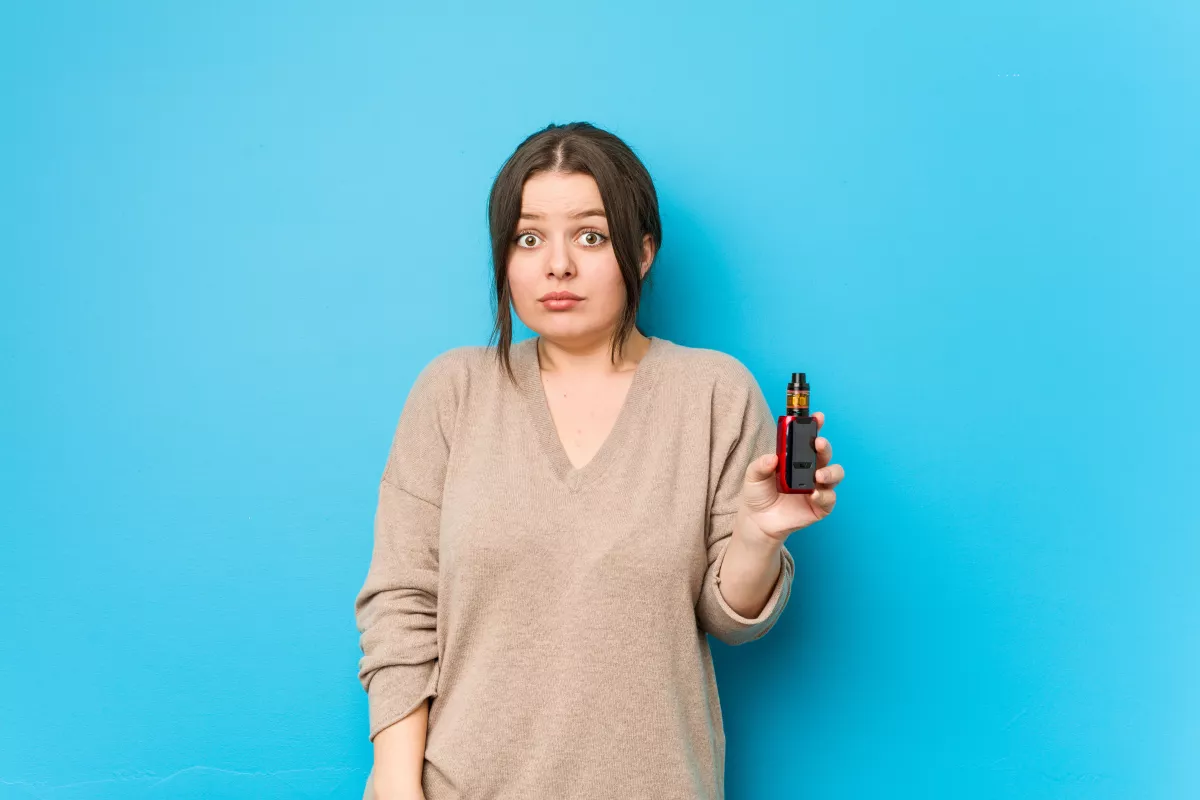 Person in sweater holding red CBD vape bottle, surprised expression, blue background.
