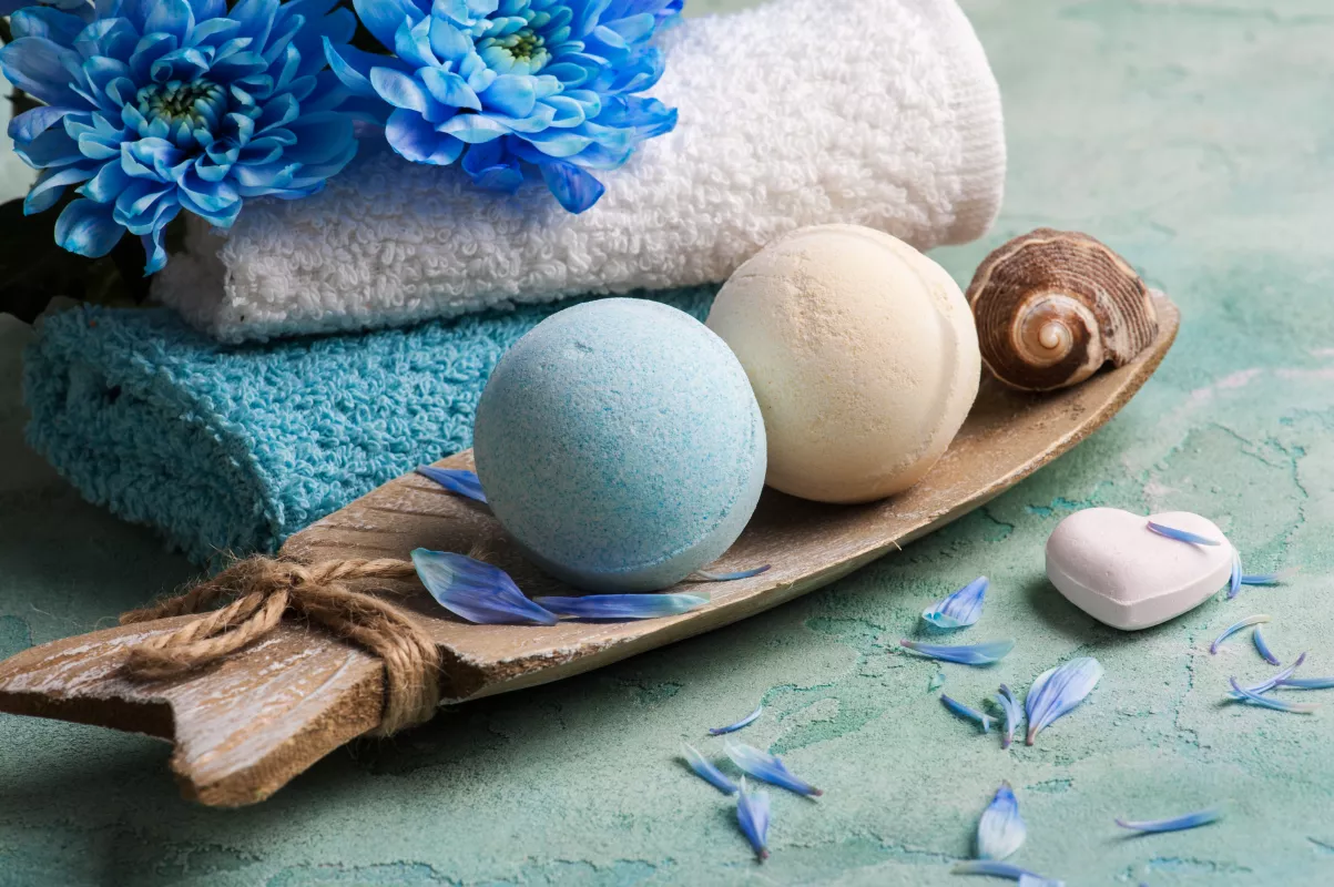 Spa day essentials with plush towels, blue flowers, and CBD-infused bath bombs for relaxation.