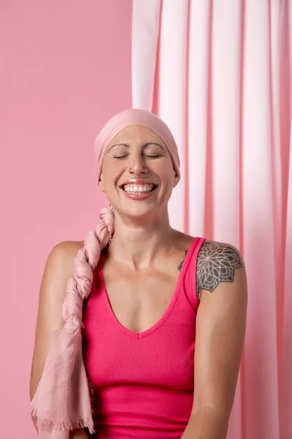 Happy person in pink with headscarf and shoulder tattoo against a pink backdrop.