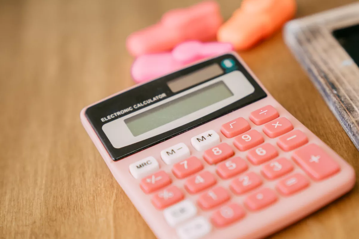 Pink calculator with white buttons on wooden desk near smartphone, modern office essentials.