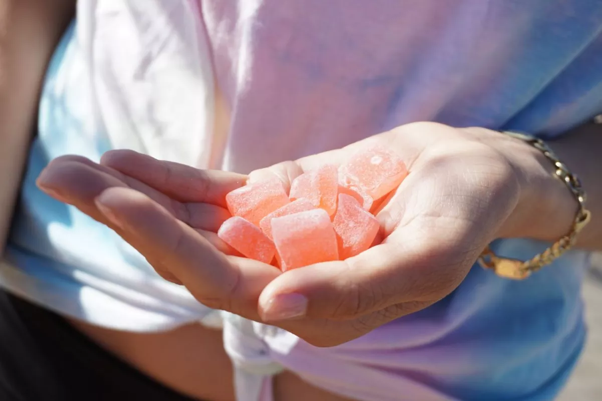Person holding pink CBD crystals against a pastel tie-dye background.