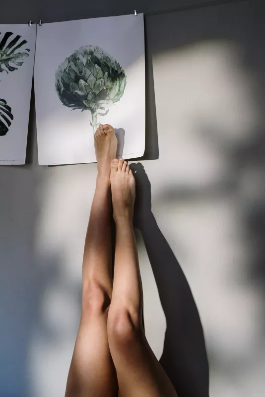 Serene wellness scene with legs against botanical art in sunlight, suggesting relaxation and CBD benefits.