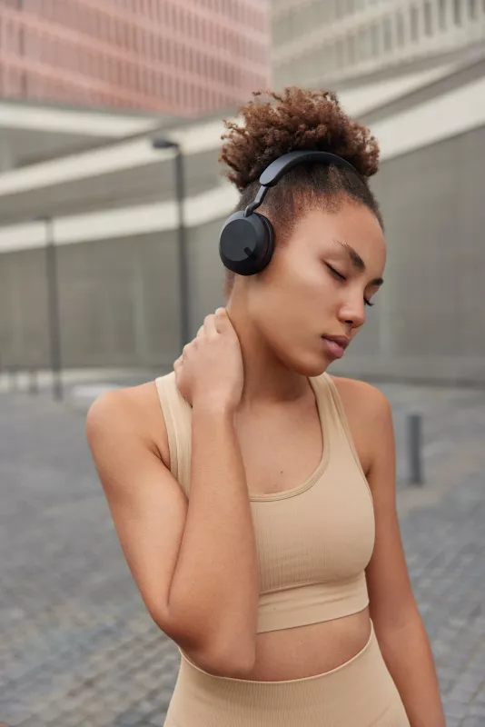 Person in beige athleisure enjoying music with headphones in a serene urban outdoor setting.