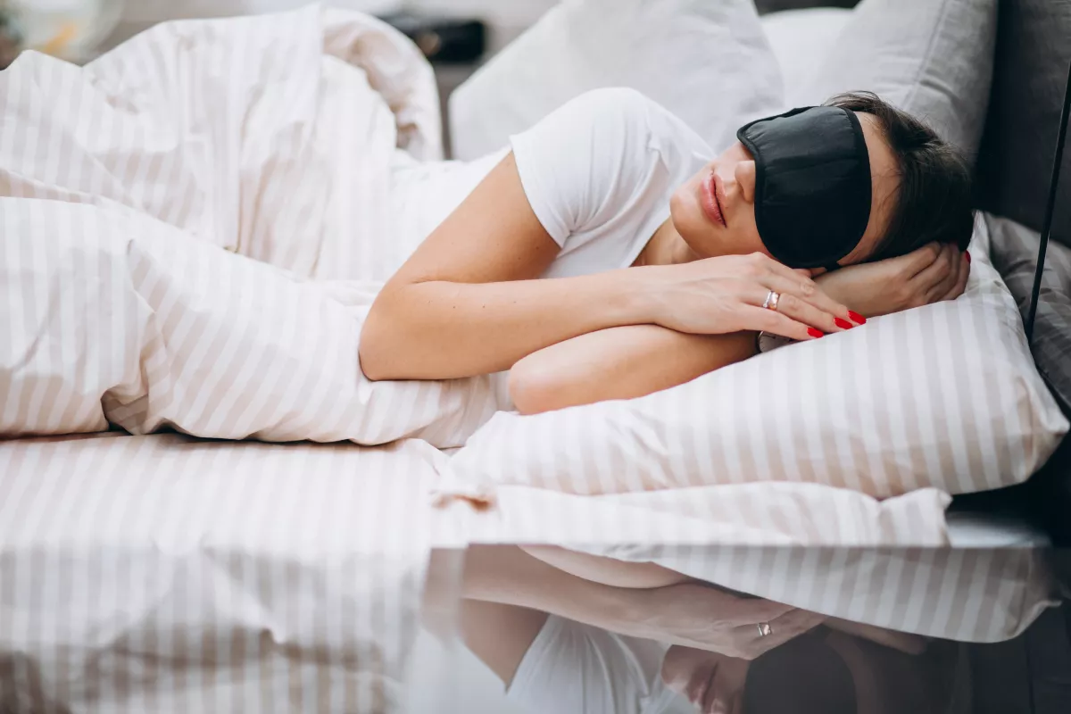 Adult sleeping peacefully with sleep mask on striped bed linens for optimal sleep hygiene.