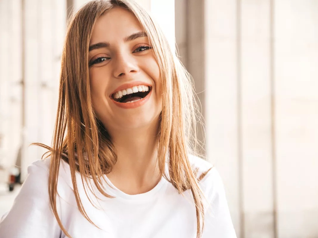 Smiling young woman in white top, joyful indoor portrait with soft lighting.