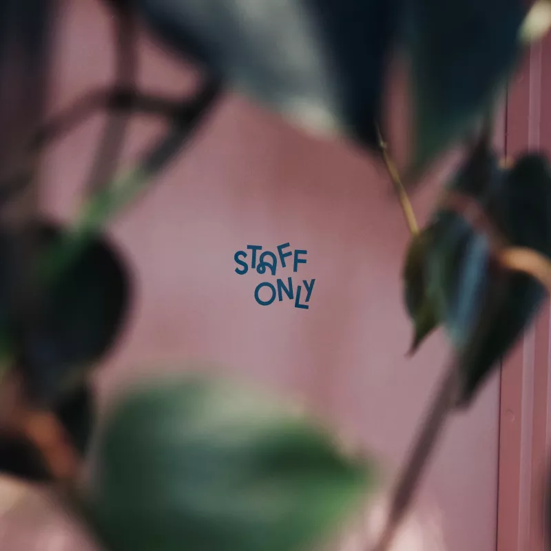 Blurred greenery frames a sharp STAFF ONLY sign on a pink backdrop, indicating restricted access.
