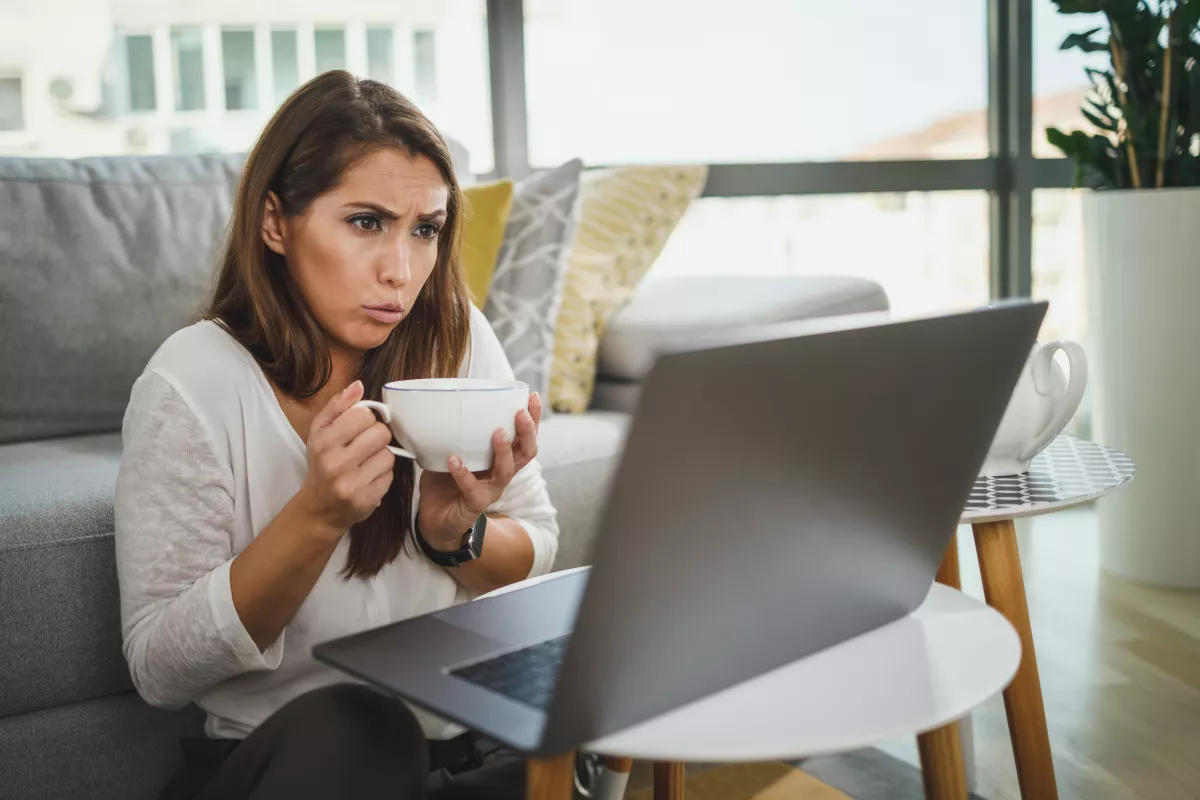 Woman sipping coffee while concentrating on laptop in modern living room.