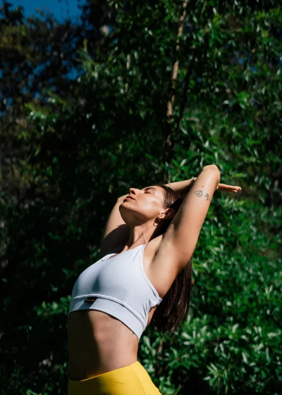 Woman in activewear enjoying sunlight in green outdoor setting.