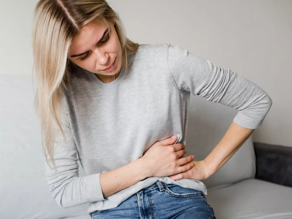 Woman in gray sweater clutching side in pain.