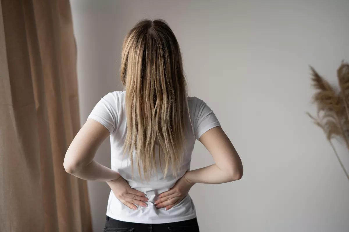 Woman with lower back pain stands against blurred background, highlighting posture relief methods.