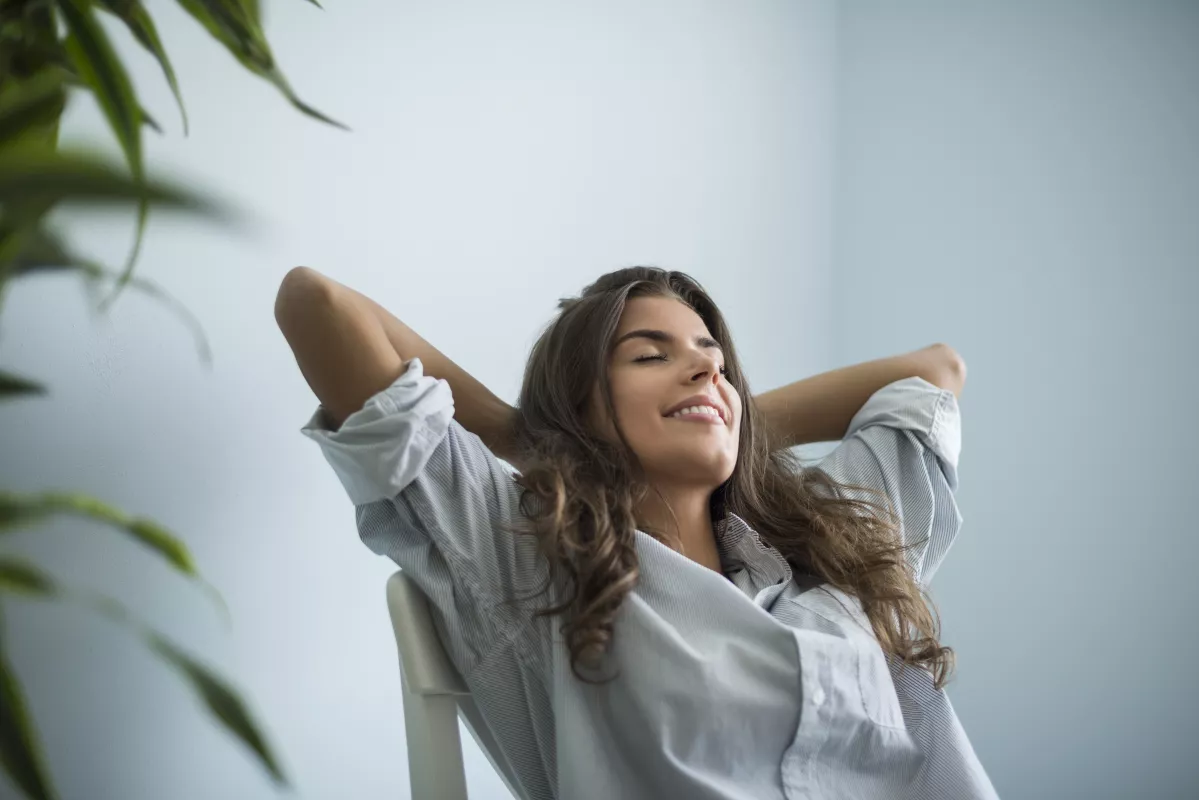 Woman in striped shirt finds tranquility, relaxing in office chair with eyes closed and serene backdrop.