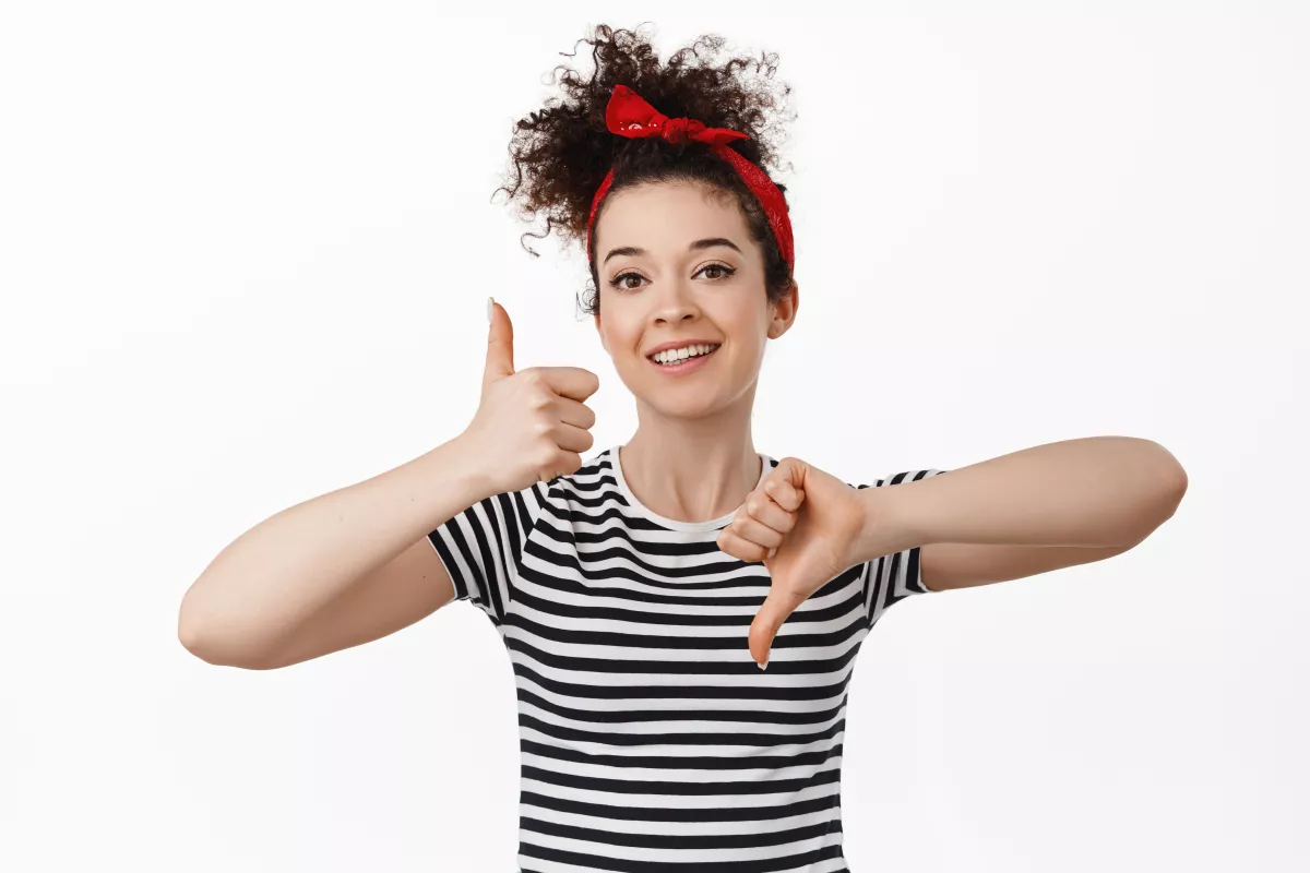 Woman smiling, giving thumbs-up and thumbs-down, deciding with striped shirt and red headband.
