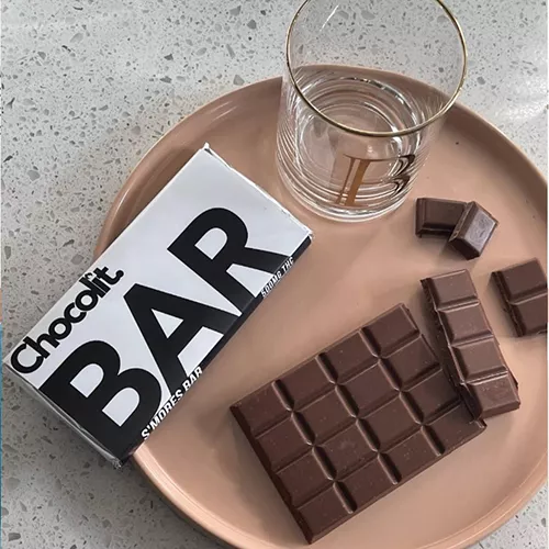 A minimalistic chocolate bar setup on a pink plate with water glass.