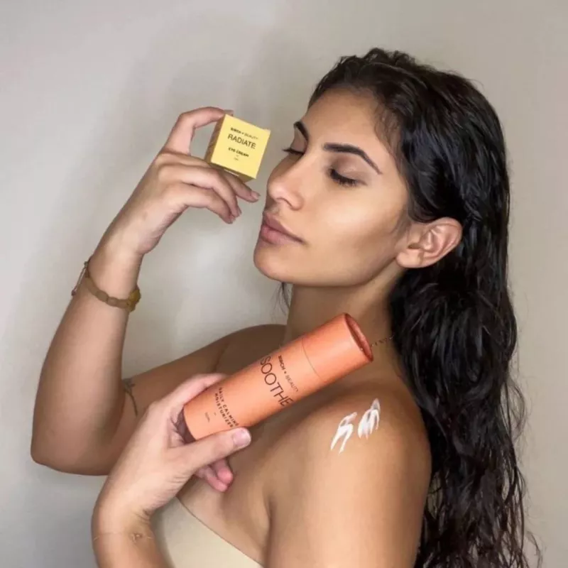 Young woman showcasing Radiate eye cream and Soothe body butter, glowing skin, serene expression.