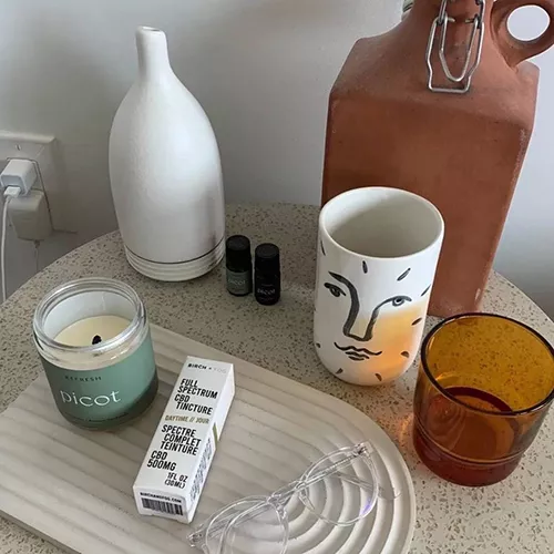 Cozy tabletop decor with jugs, candle, essential oils, artistic cup, and glasses on a tray.