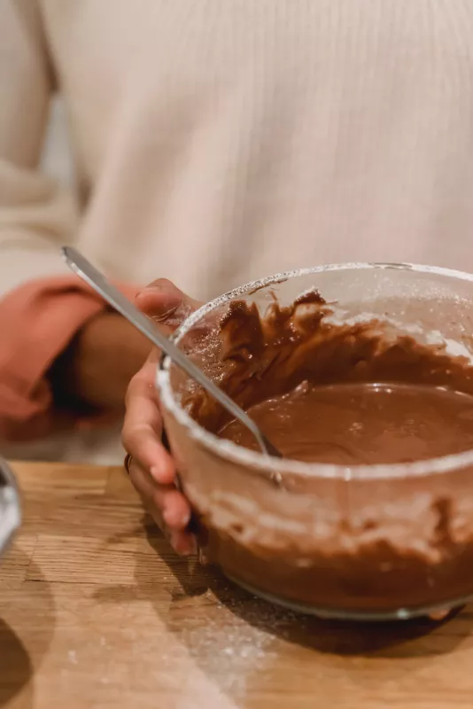 Person mixing chocolate batter in a bowl on a wooden surface, cozy home baking scene.