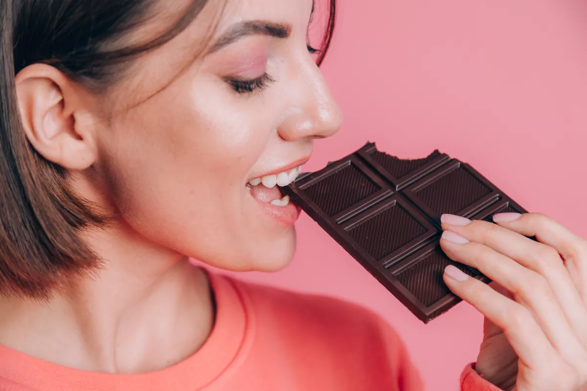 Woman indulging in a bite of luxurious dark chocolate, evoking a sense of delight and satisfaction.