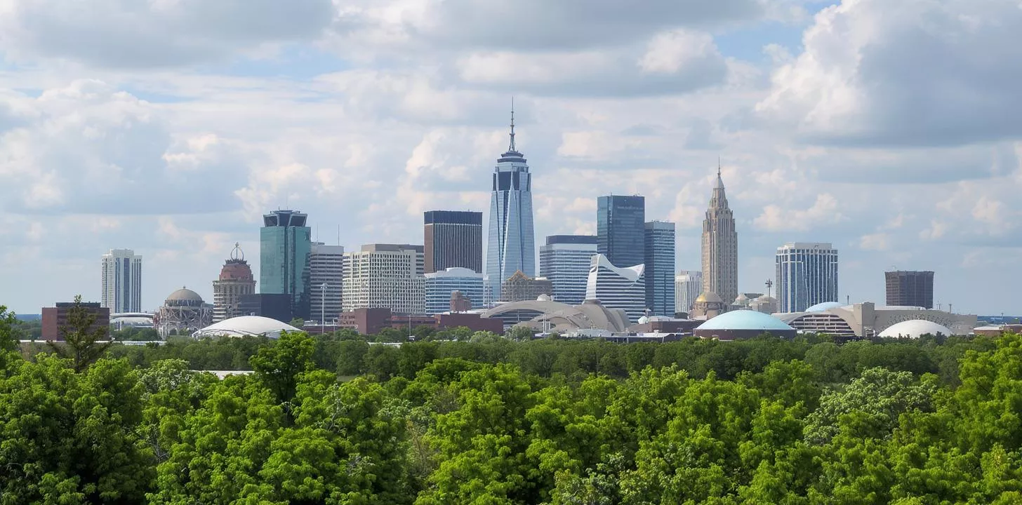Modern city skyline with diverse architecture, lush green park, and partly cloudy sky.