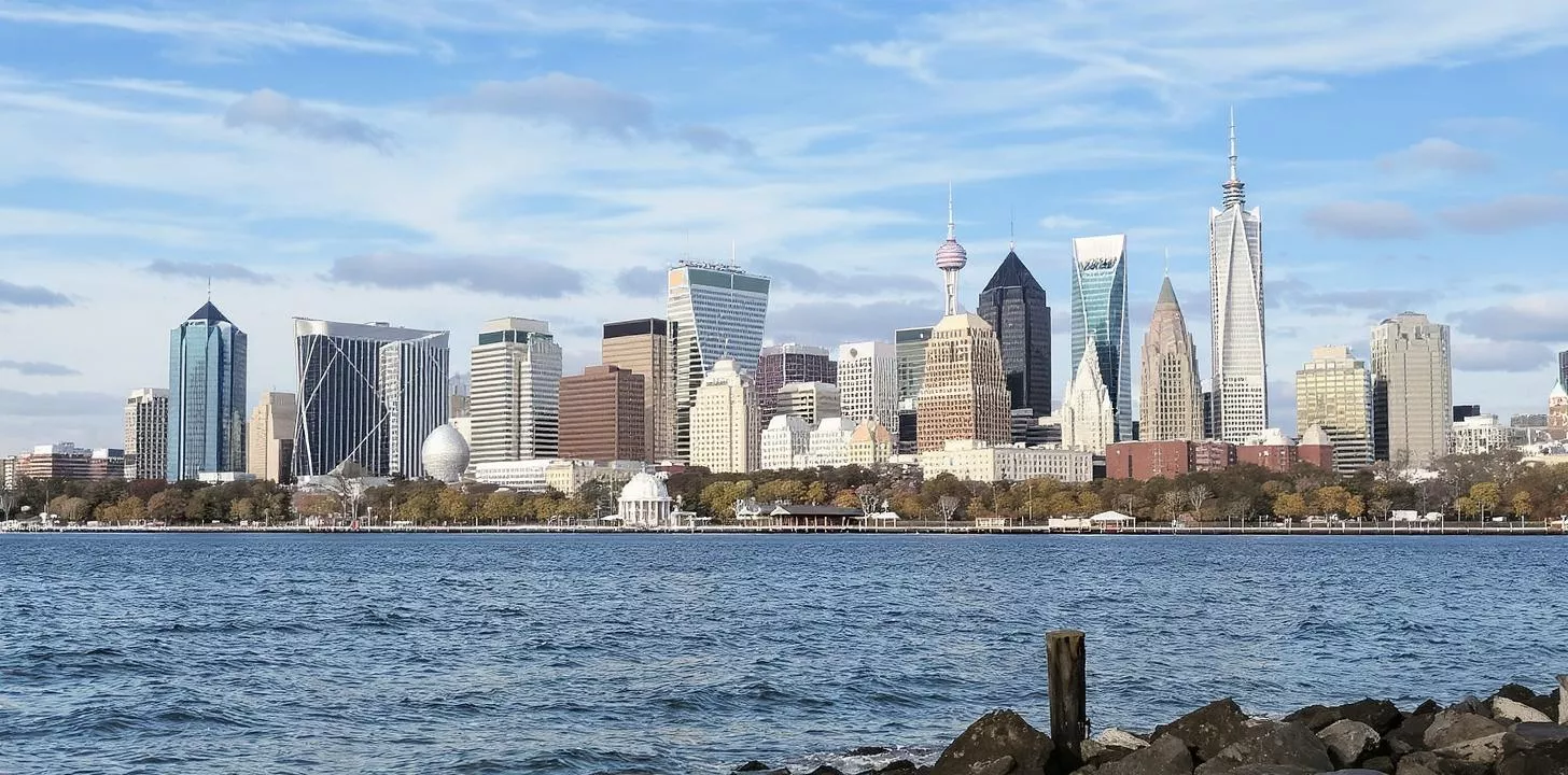 Stunning skyline: modern skyscrapers, serene water, autumn trees, and a striking domed structure.