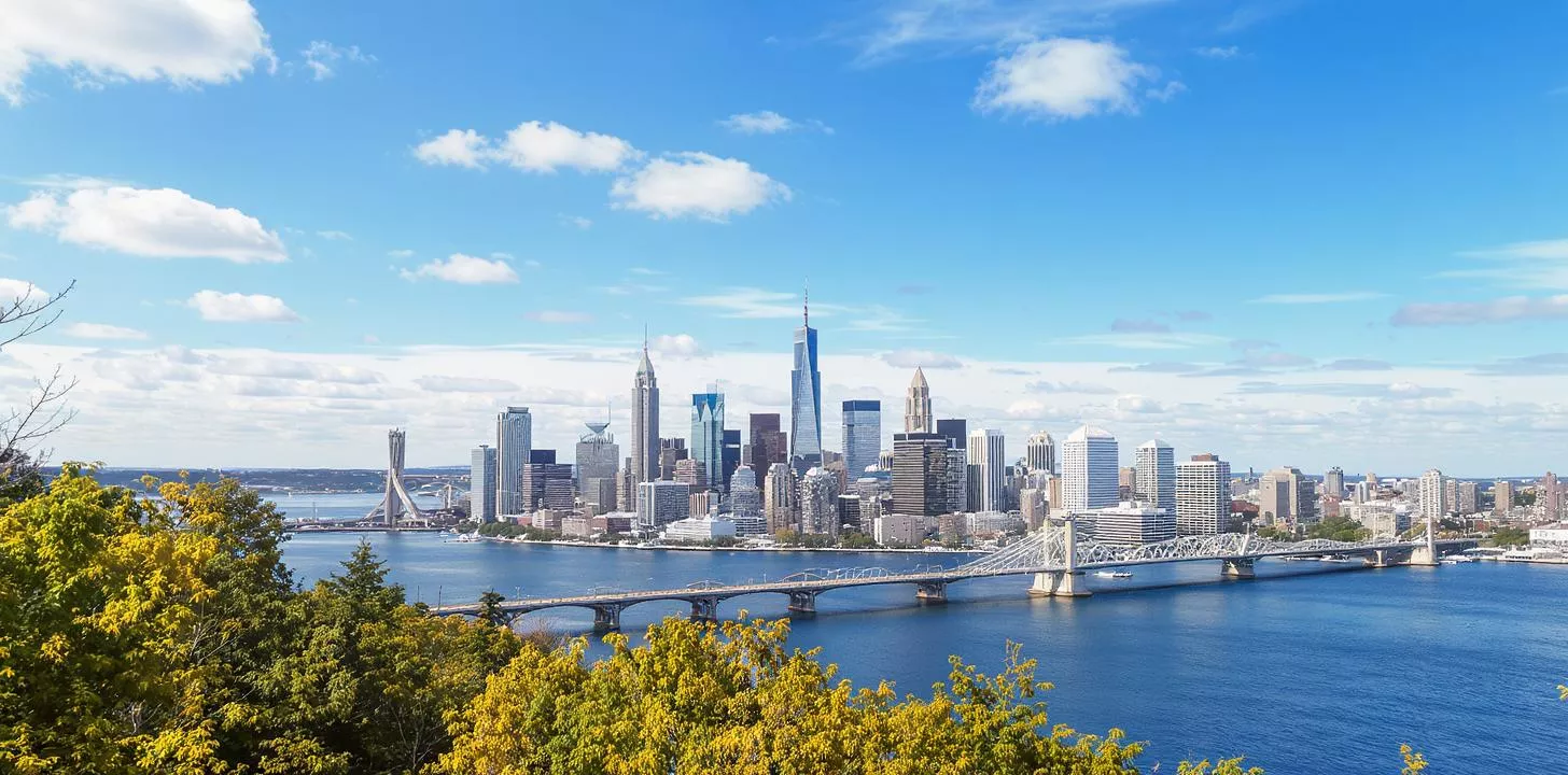 Urban skyline with skyscrapers, lush greenery, and a scenic bridge over water in autumn.