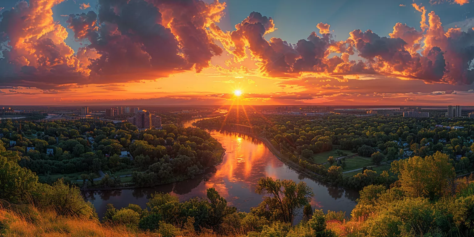 Sunset over river and cityscape with vibrant colors and lush landscape.