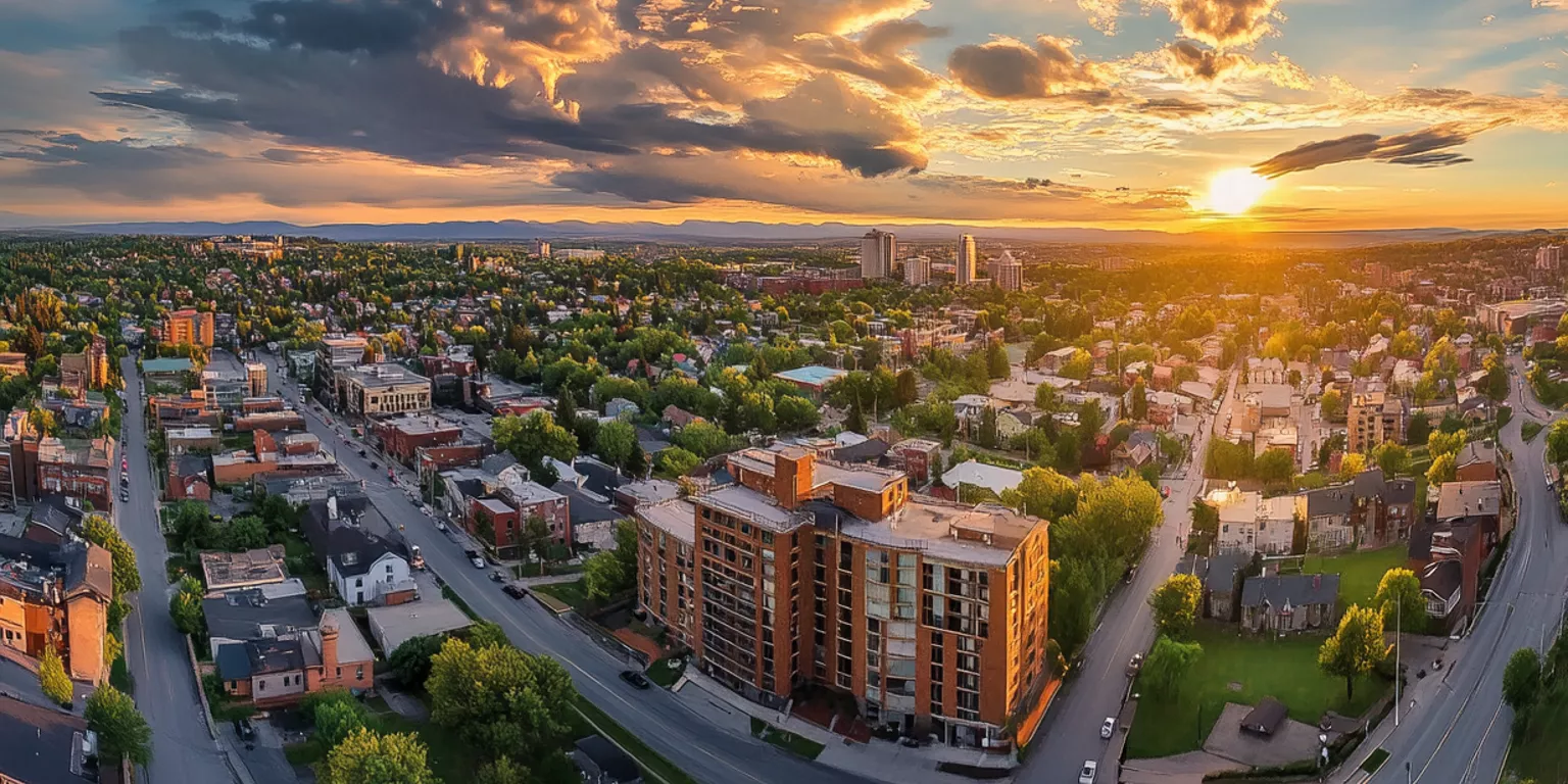 Aerial view of city at sunset with buildings, roads, and lush greenery.