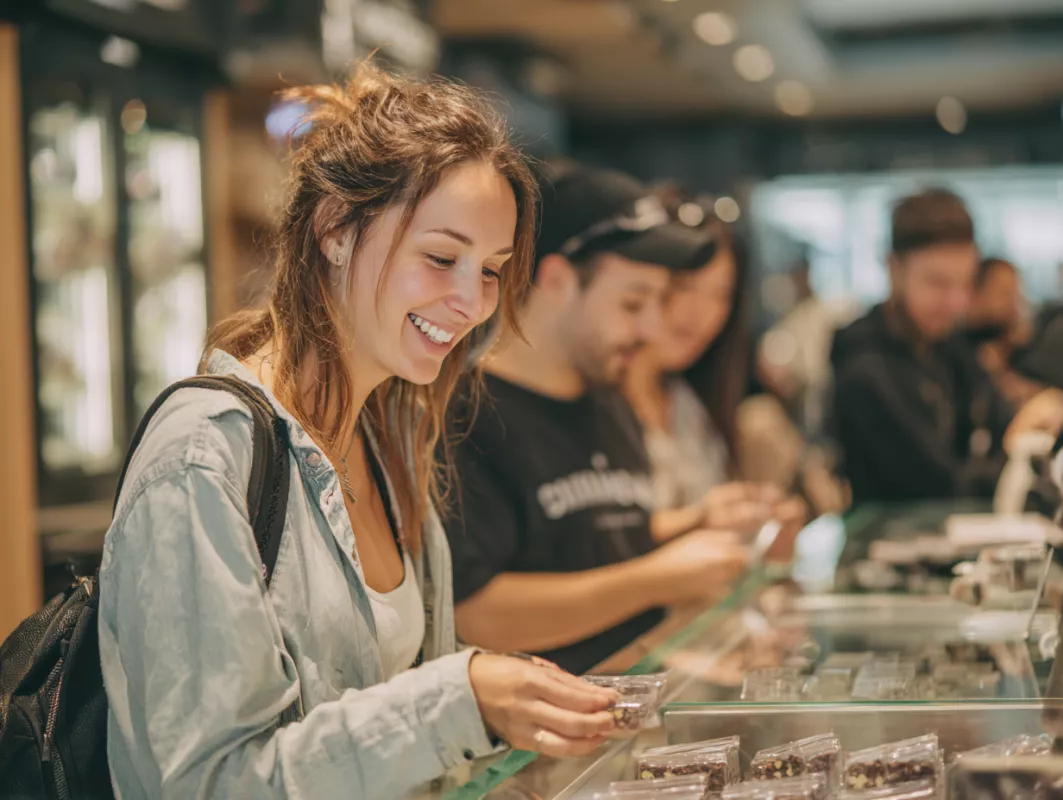 Young woman shopping at bustling cannabis dispensary, examining products on display.