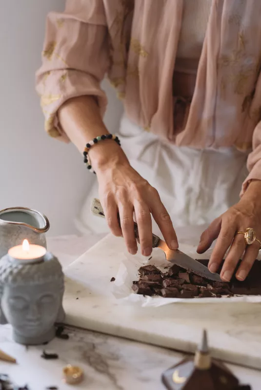 Elderly hands chop dark chocolate on marble for homemade CBD dosage, serene kitchen setting.
