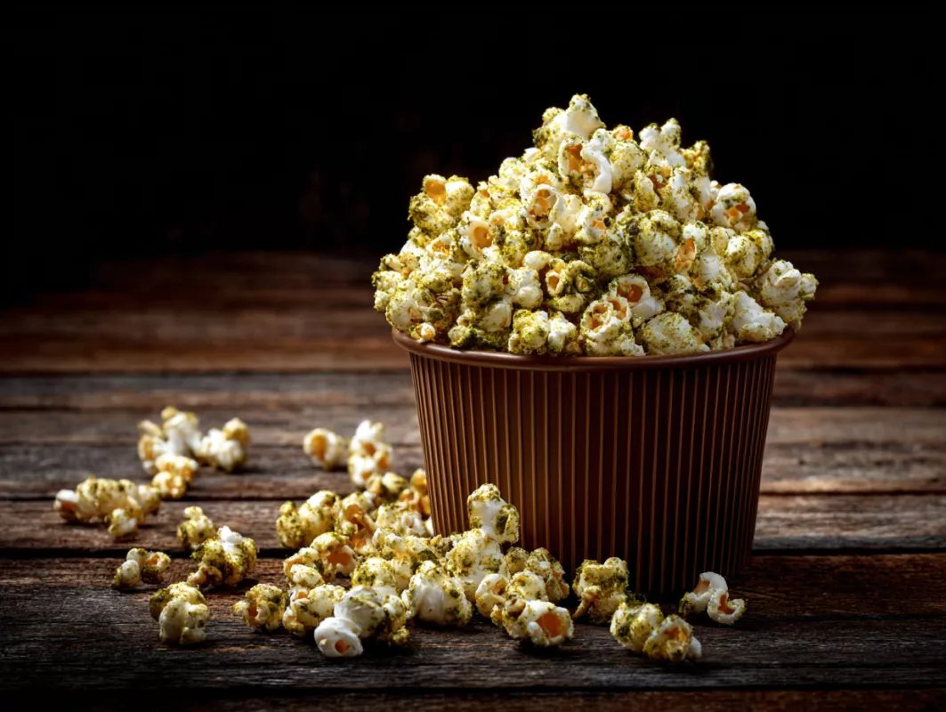 Bowl of seasoned popcorn with herbs on a rustic wooden table.