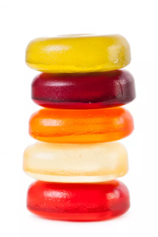 Colorful stack of five hard candy lozenges with glistening, translucent appearance on white background.