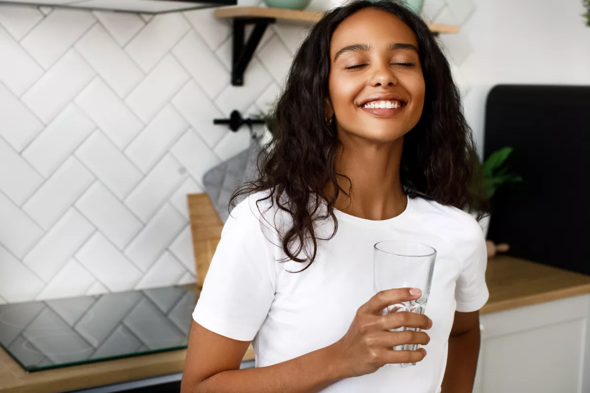 Woman sipping water in a chic kitchen with modern decor.