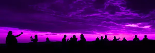 Silhouetted figures admire vibrant sunset sky with pink and purple hues.