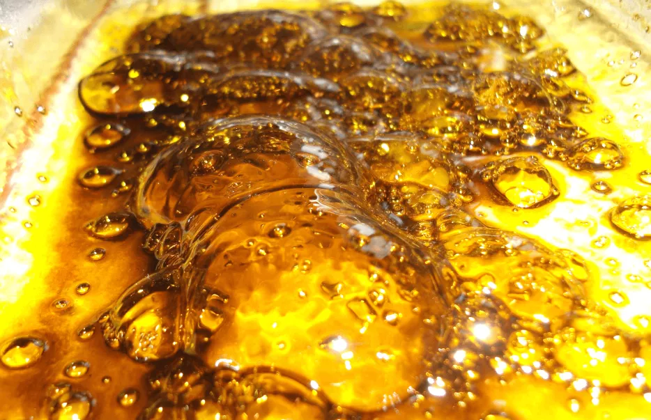 Amber butane hash oil close-up with glossy surface, bubbles, and ripples.