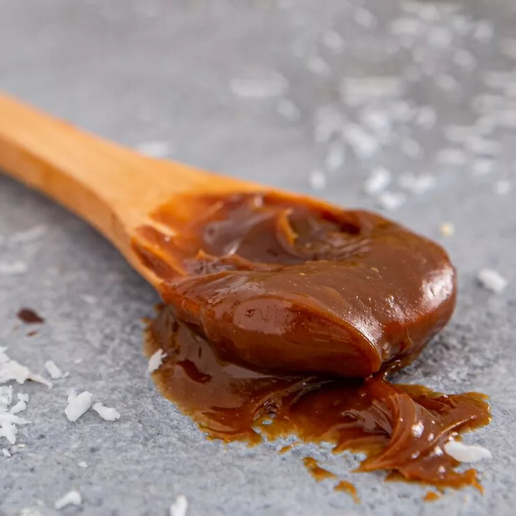 Glossy salted caramel on spoon with sea salt crystals against grey background.