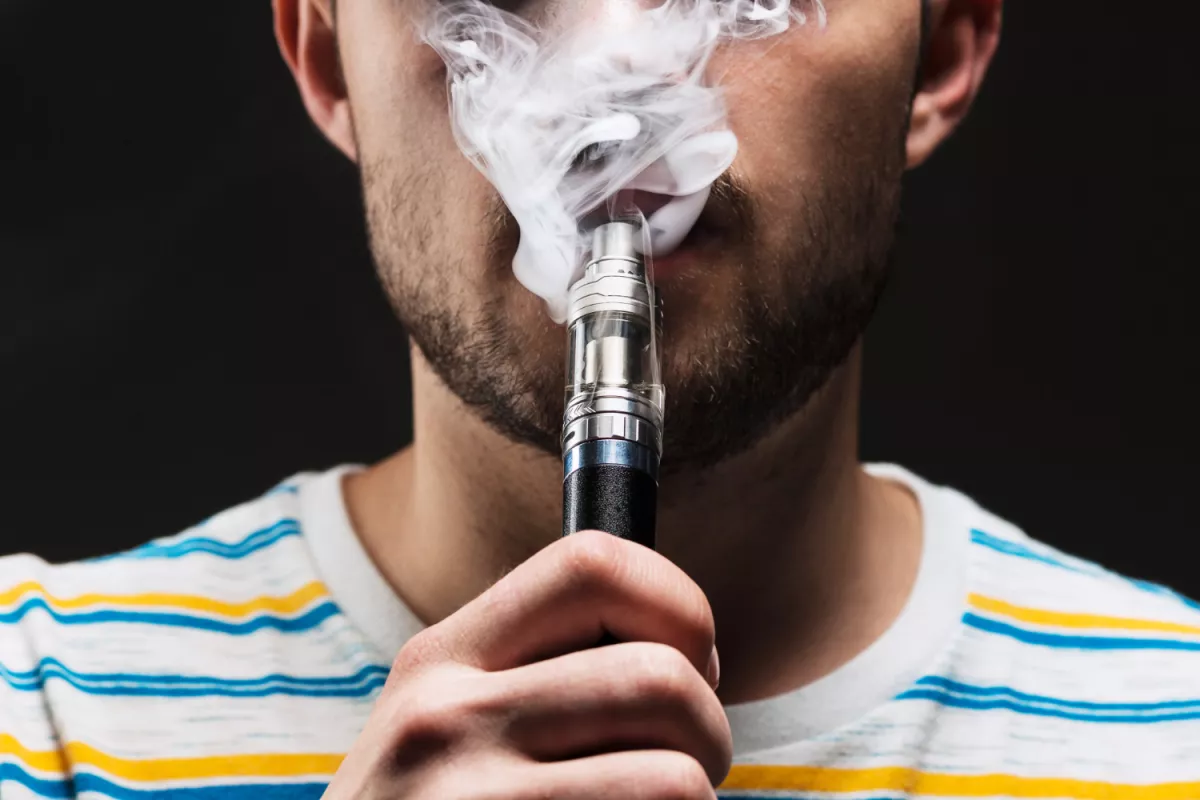 Man exhaling vapor from e-cigarette, close-up against black background.
