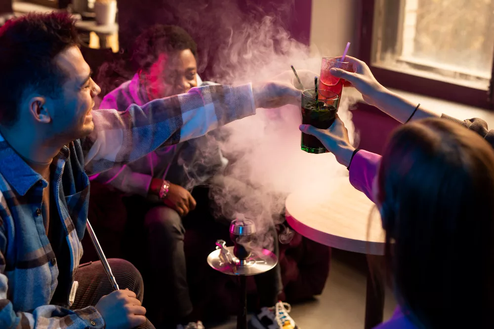 Friends clinking glasses in a smoky hookah lounge.