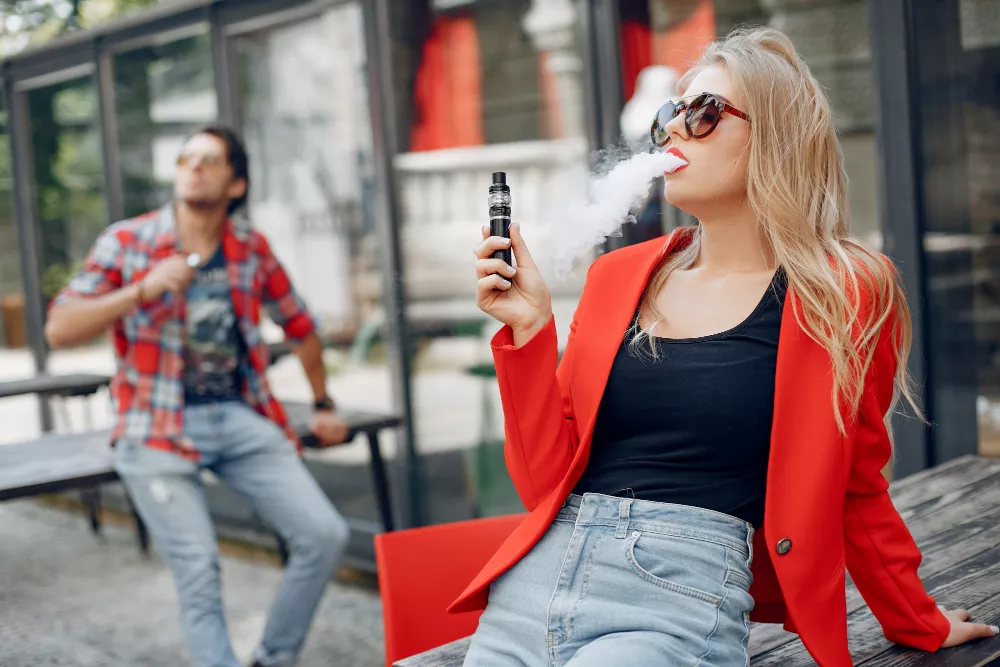 Stylish woman and man vaping outdoors in a modern city setting.