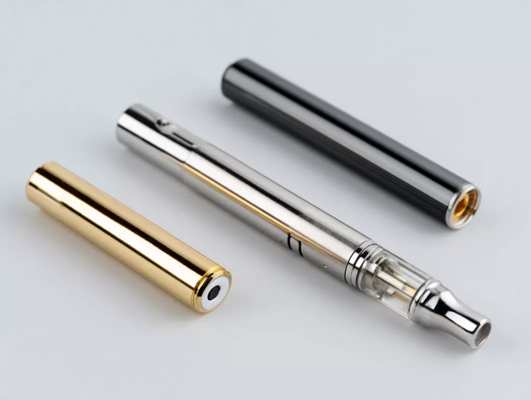 Sleek vape pen with gold and black interchangeable battery components on a gray background.