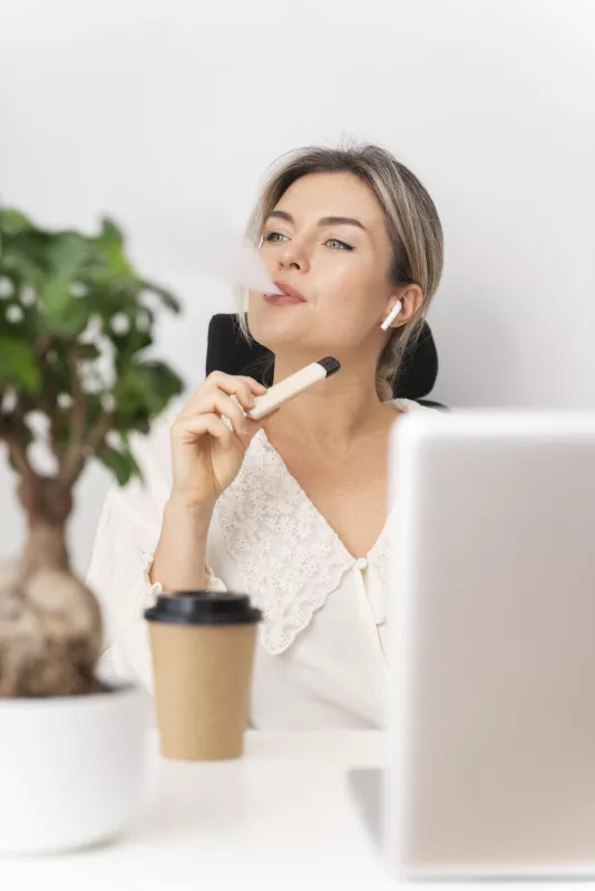 Woman contemplating work at desk with laptop, coffee, and plant in a casual office setting.