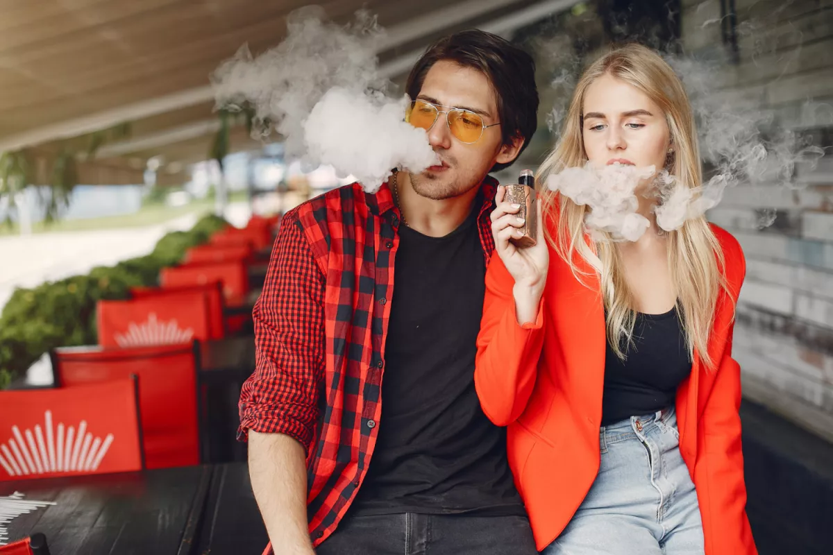 Young couple enjoys vaping at an outdoor café.